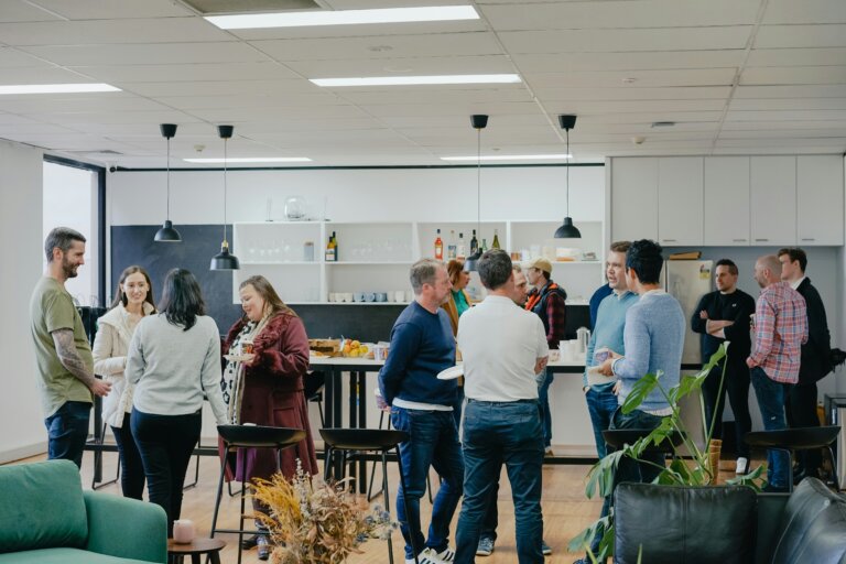 A room of people networking in an open spacious kitchenette. They are in groups chatting.