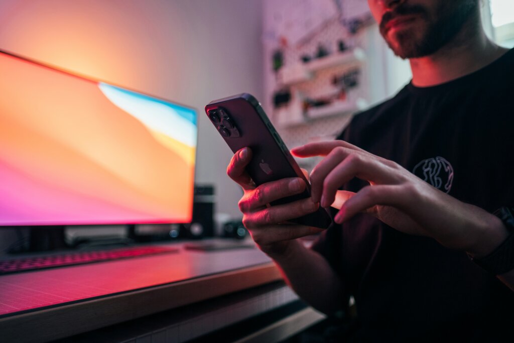 A man in front of a monitor looking down at his smartphone.