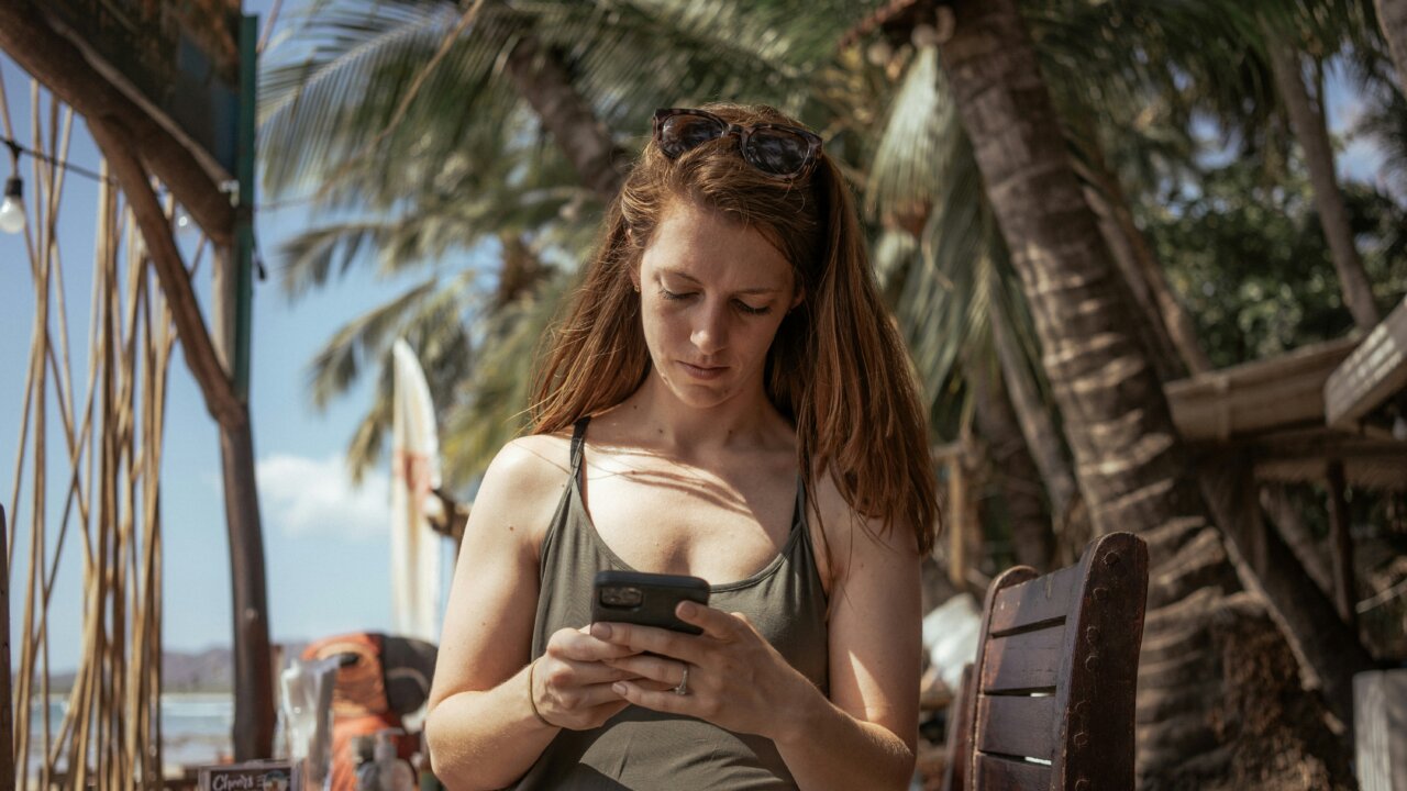 A woman seemingly on holiday but checking messages on her phone. She looks serious.