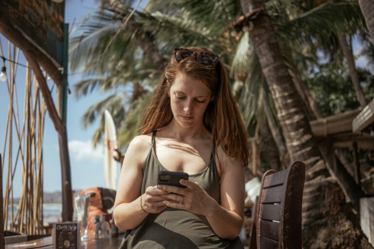 A woman seemingly on holiday but checking messages on her phone. She looks serious.