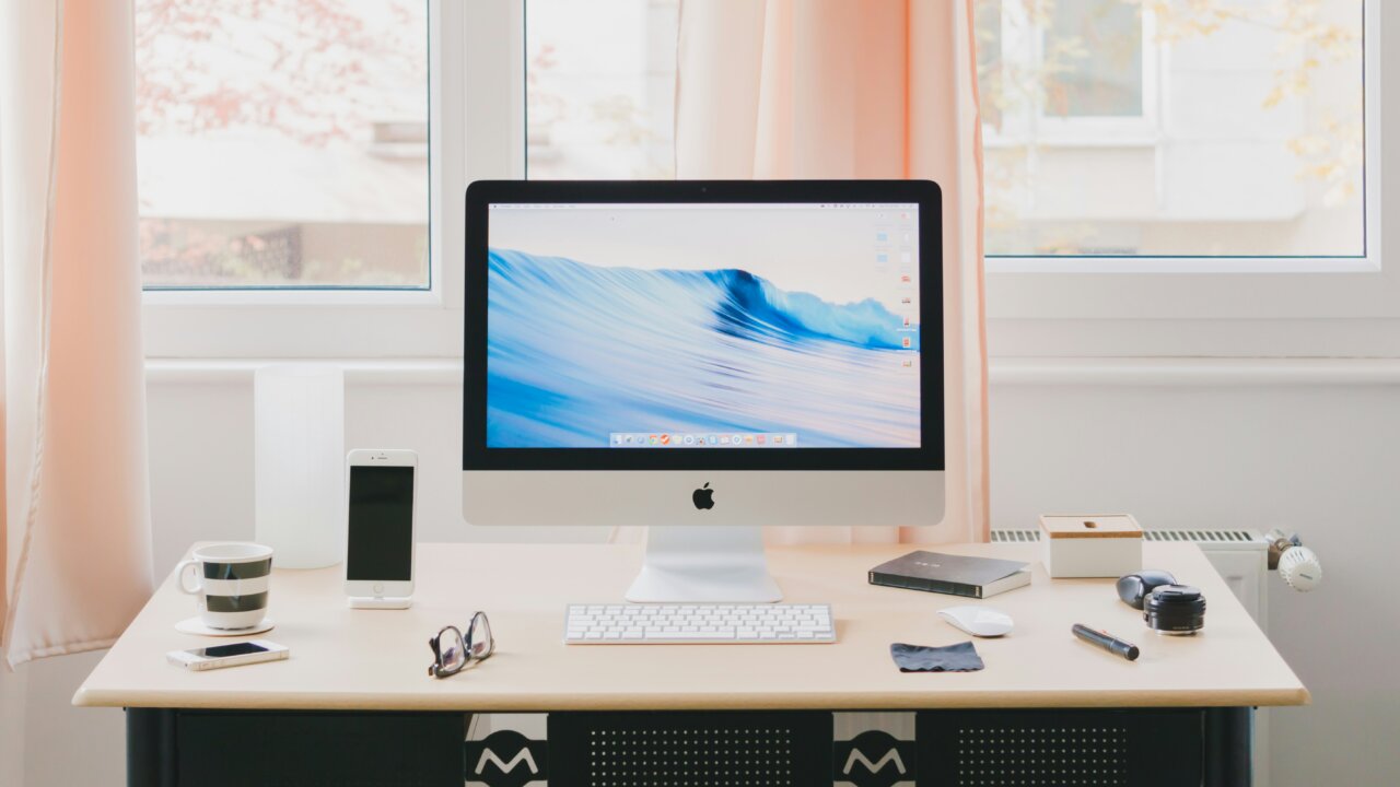 An asthetic desk scene with a older generation imac, iphone and other peripherals neatly laid out.
