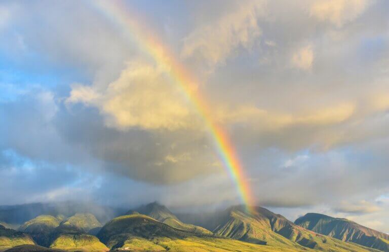 An image of a rainbow in a cloudy sky above some green hills.